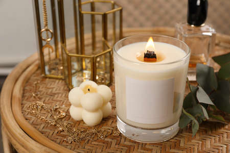 Burning soy candle, perfume and stylish accessories on wicker table indoorsの写真素材
