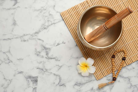 Golden singing bowl with mallet, beads and flower on white marble table, flat lay. Space for textの写真素材