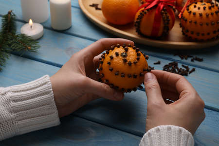 Woman decorating fresh tangerine with cloves at light blue wooden table, closeupの写真素材