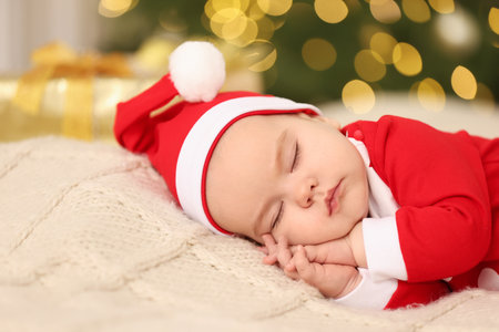 Cute baby in Christmas costume sleeping on knitted blanket against blurred festive lights. Winter holidayの写真素材