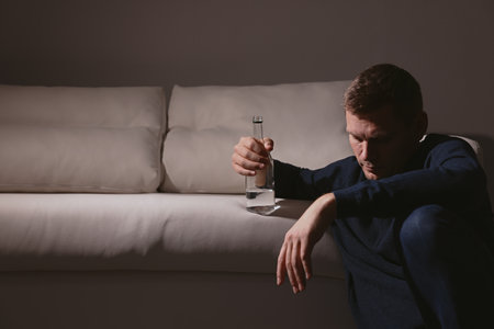Addicted man with alcoholic drink near sofa indoors. Space for textの写真素材