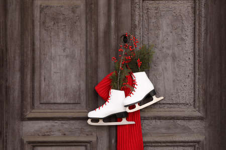 Pair of ice skates with Christmas decor hanging on old wooden door