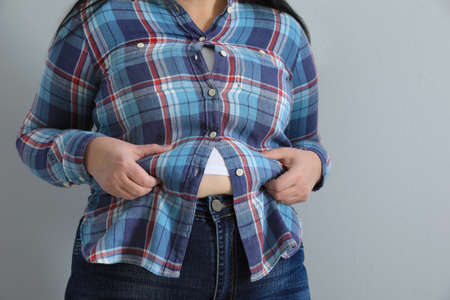 Overweight woman in tight shirt on light gray background, closeup