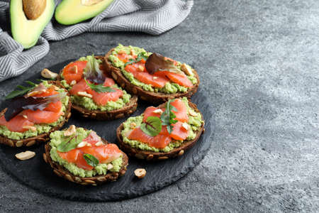 Delicious sandwiches with salmon, avocado and herbs on gray table. Space for text