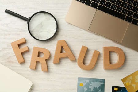 Word Fraud made of wooden letters, credit cards, laptop and magnifying glass on white table, flat layの写真素材