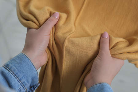 Woman touching clothes made of soft yellow fabric indoors, closeup