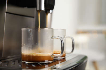 Espresso machine pouring coffee into glass cups against blurred background, closeup. Space for textの写真素材