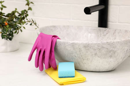 Sponge, rag and rubber gloves near sink in bathroom