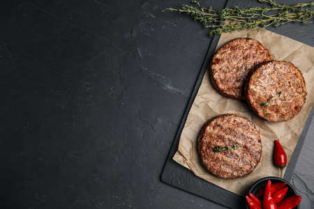 Tasty grilled hamburger patties, thyme and chili peppers on black table, flat lay. Space for textの写真素材