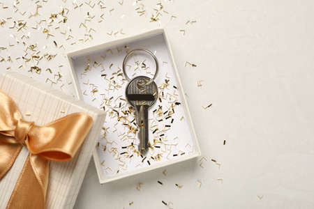 Key with confetti in gift box on white table, flat lay and space for text. house warming party