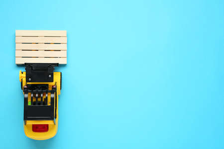 Toy forklift with wooden pallet on light blue background, top view. Space for text