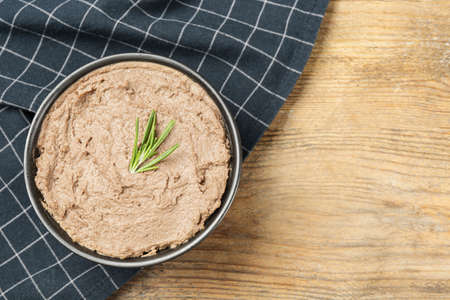 Tasty liver pate with rosemary in bowl on wooden table, top view. Space for textの写真素材