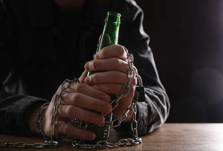 alcohol addiction. Man chained with bottle of beer at wooden table, closeupの写真素材
