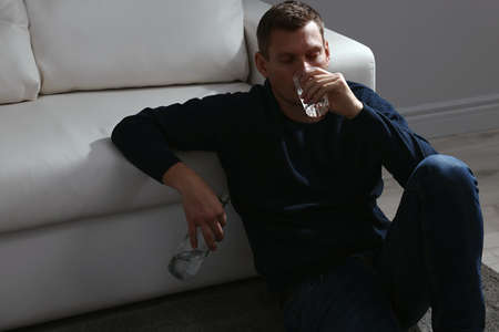 Addicted man drinking alcohol near sofa indoors