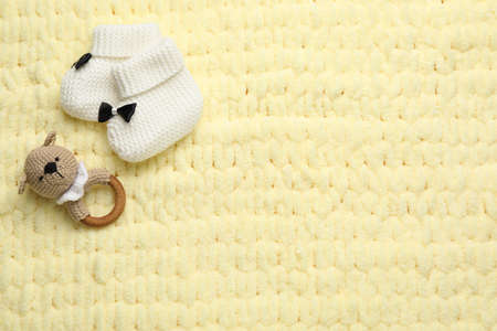 Cute baby booties and toy on yellow knitted fabric, flat lay. Space for textの写真素材