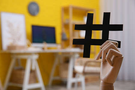 Wooden mannequin hand with paper hashtag symbol indoors. Space for textの写真素材