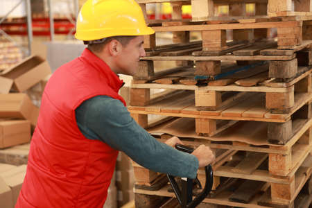 Worker moving wooden pallets with manual forklift in warehouse