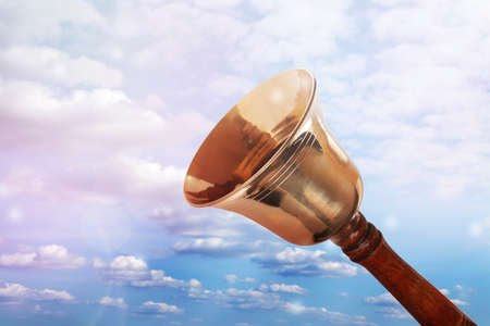 Shiny school bell with wooden handle against blue skyの写真素材