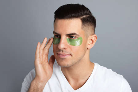 Man applying green under eye patch on gray background