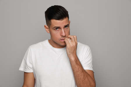 Man biting his nails on gray background. Bad habit