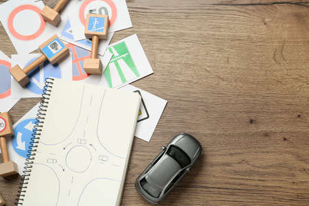 Many different road signs, notebook and toy car on wooden background, flat lay with space for text. driving schoolの写真素材