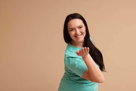Beautiful overweight woman with charming smile on beige background. Space for text