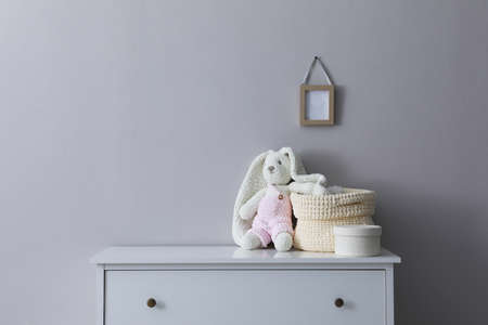 Child's toy and wicker basket on chest of drawers near light gray wall indoors
