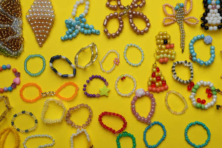 Beautiful handmade beaded jewelry and crafts on yellow background, flat lay
