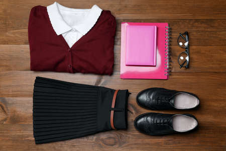Stylish school uniform, glasses and notebooks on wooden background, flat layの写真素材