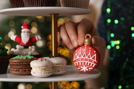 Woman taking Christmas macaron from stand against blurred festive lights, closeupの写真素材