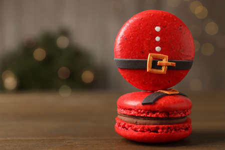 Beautifully decorated Christmas macarons on wooden table against blurred festive lights, space for textの写真素材