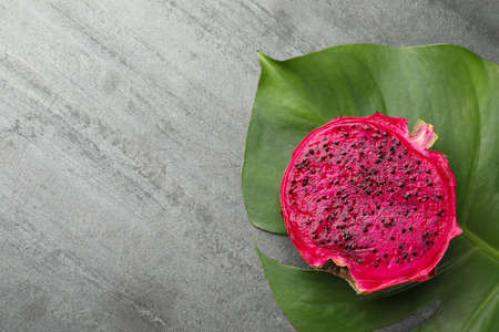 Delicious cut red pitahaya fruit and green leaf on gray table, flat lay. Space for textの写真素材