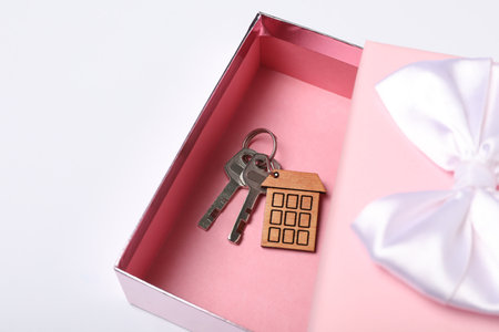 Keys with trinket in shape of house and gift box on white background. house warming party