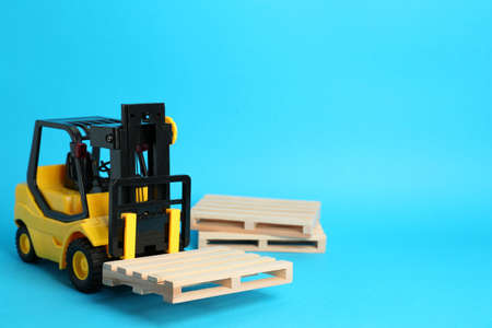 Toy forklift and wooden pallets on light blue background, space for textの写真素材