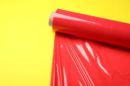 Roll of red plastic stretch wrap on yellow background. Space for text