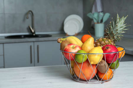 Metal basket with different ripe fruits on white wooden table in kitchen. Space for textの写真素材