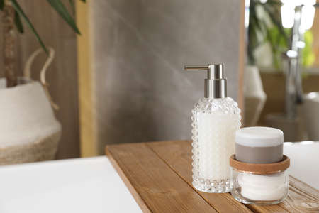 White tub with soap dispenser, cotton pads and jar in bathroom, space for text. interior design
