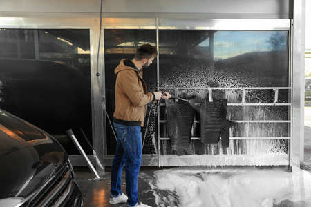 Man cleaning auto mats with high pressure water jet at self-service car washの写真素材