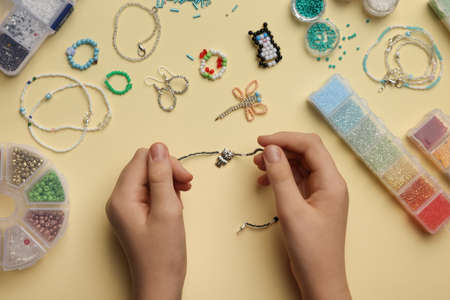 Girl making beaded jewelry on beige background, top viewの写真素材