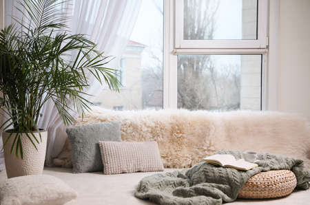 Comfortable lounge area with faux fur and pillows near window in roomの写真素材