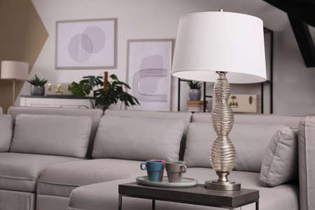 Comfortable sofa in living room, focus on table with cups and lampの写真素材