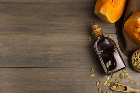 Glass bottle of oil with cut pumpkin and seeds on wooden table, flat lay. Space for textの写真素材