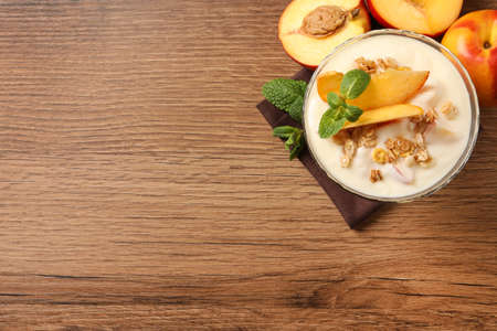 Tasty peach yogurt with granola, mint and pieces of fruit in dessert bowl on wooden table, flat lay. Space for textの写真素材