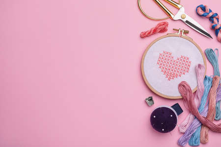 Flat lay composition with embroidery and different sewing accessories on pink background. Space for...