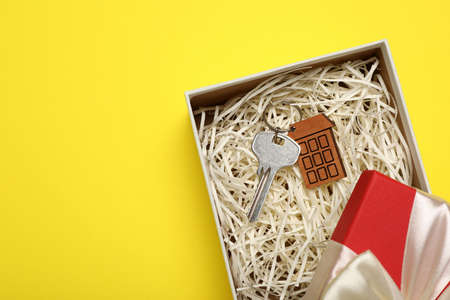 Key with trinket in shape of house on yellow background, top view and space for text. house warming...