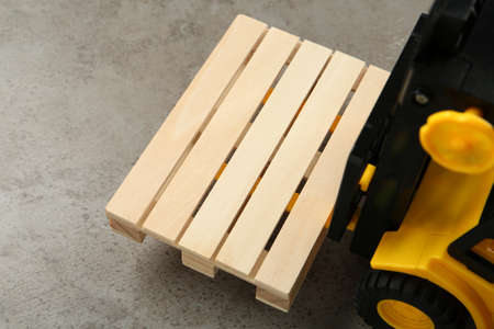 Toy forklift with wooden pallet on light gray table, closeup