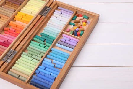 Set of soft pastels in box on white wooden table, space for text. drawing material