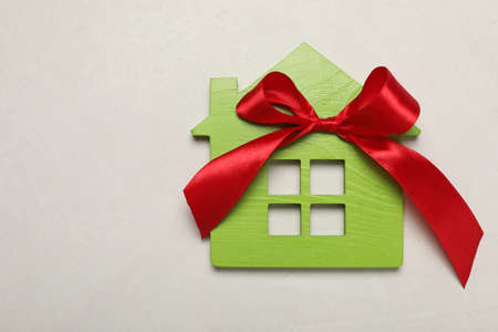Wooden house model with red bow on white table, top view and space for text. house warming partyの写真素材