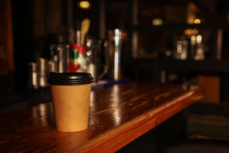 Paper coffee cup on wooden table in cafe. Space for text