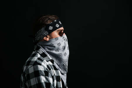 Fashionable young man with bandana covering his face on black background, space for textの写真素材